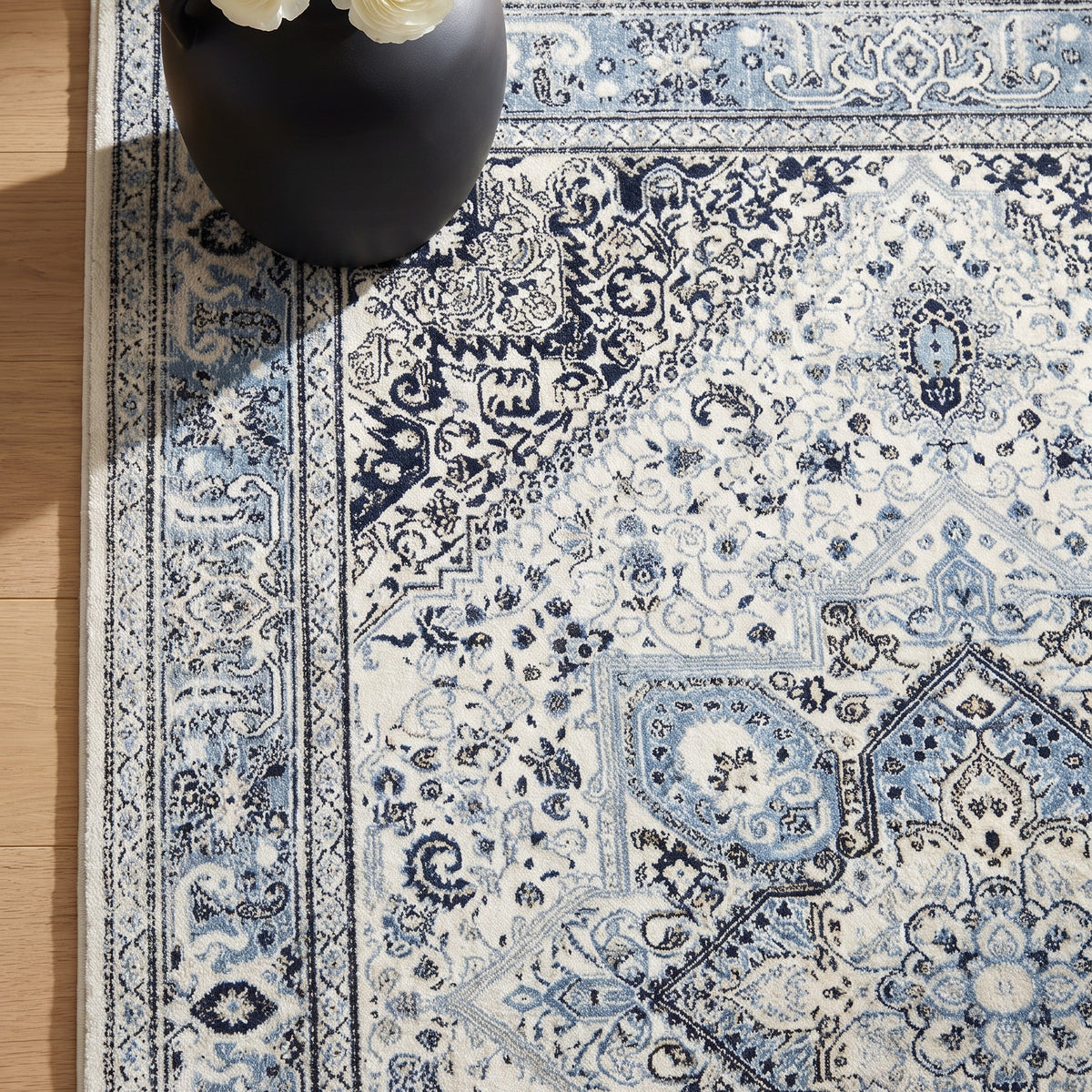Darya rug corner with a black ceramic vase of white ranunculus