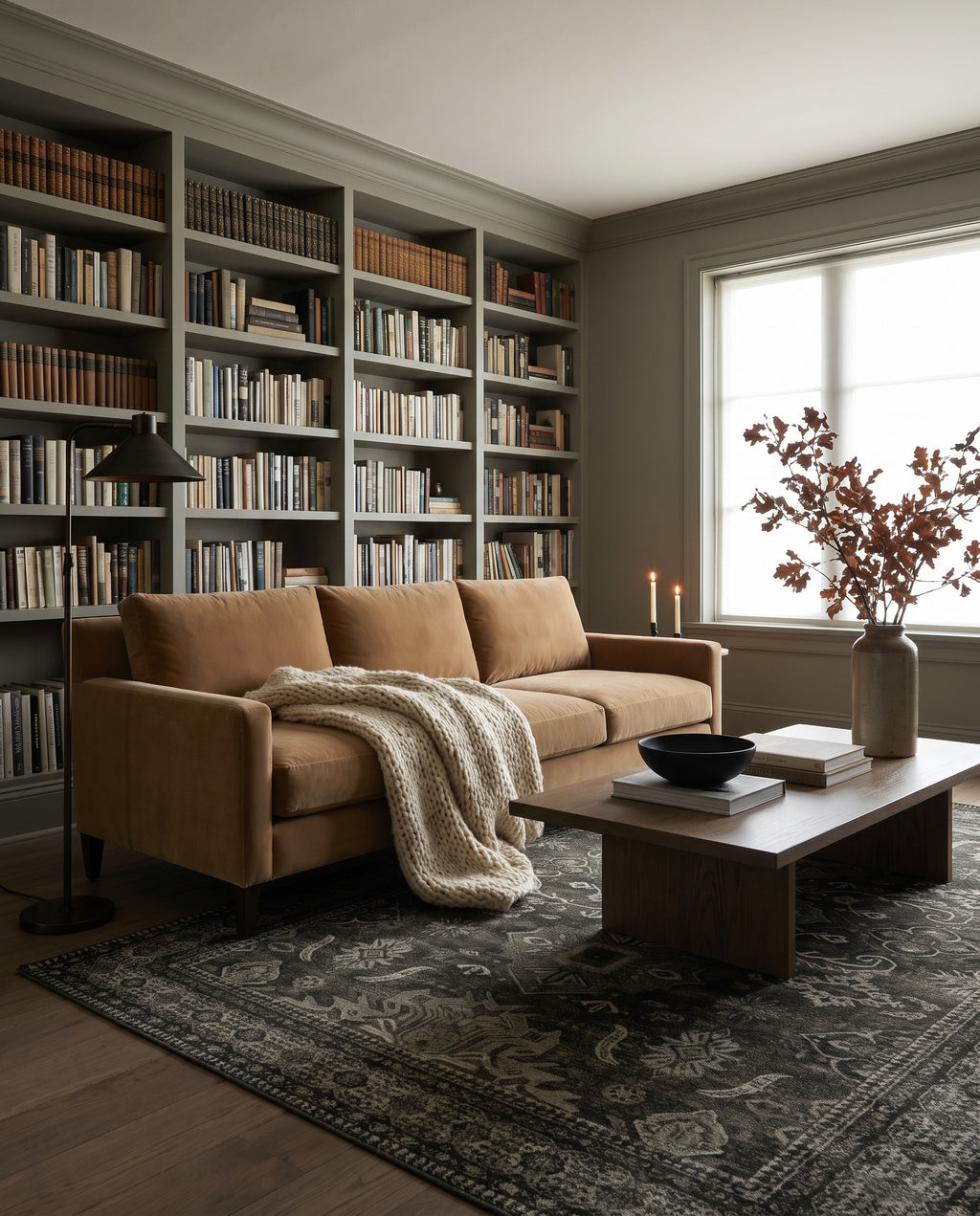 Shabnam Charcoal & Olive rug in a moody living room with a wall of books and a camel velvet sofa