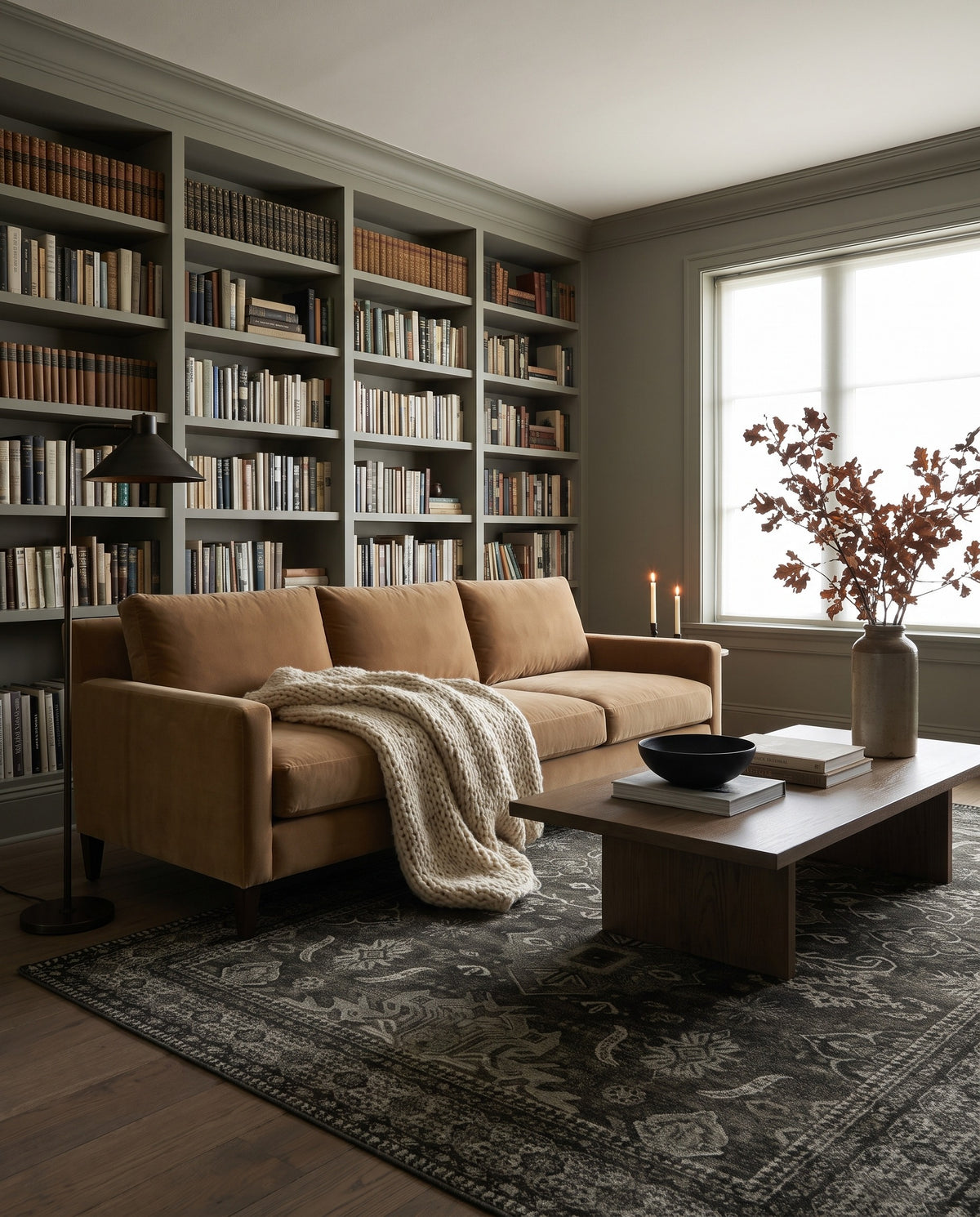 Shabnam Charcoal & Olive rug in a moody living room with a wall of books and a camel velvet sofa